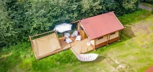 Luftaufnahme der Cozy Lodge mit rotem Dach und Veranda, der Teeny Lodge daneben und einer Hängematte auf dem Rasen